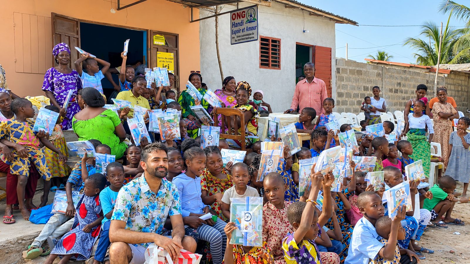Des dizaines d'enfants brandissent leurs kits scolaires devant le siège de l'ONG Handi Espoir et Amour